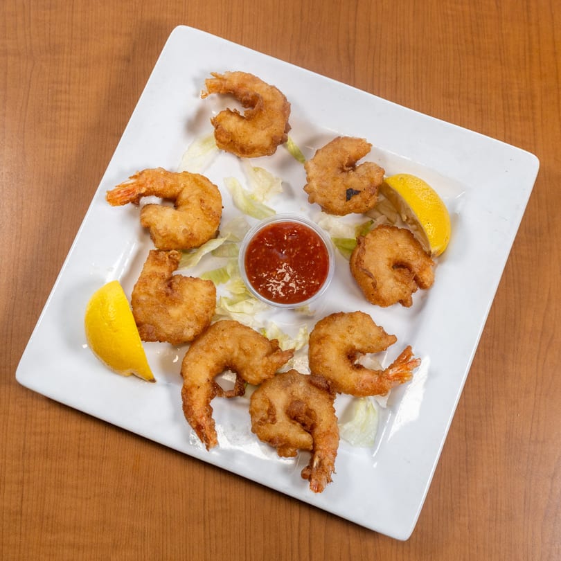 Plate of golden-fried shrimp with cocktail sauce, lemon wedges, and lettuce on a wooden table.